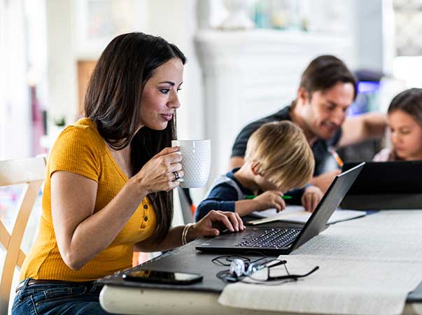 Mother works on laptop while father plays with children in background