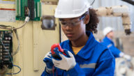 Electrical technician wearing a hard hat testing a circuit board with gage