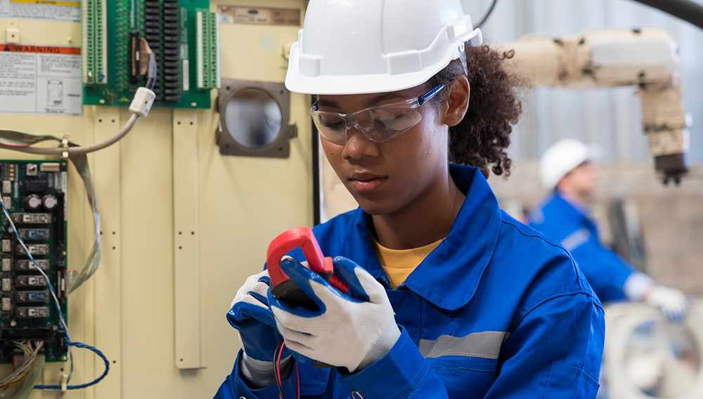 Electrical technician wearing a hard hat testing a circuit board with gage