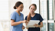 2 nurses looking over a chart in a hospital hallway
