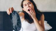 Yawning woman holds up a sleep mask