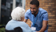 Smiling male nurse greeting an older woman in a wheelchair