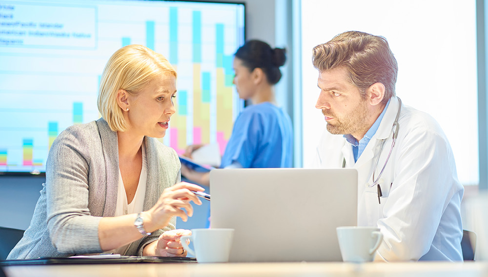 Health care financial manager going over figures on a laptop with a physician