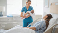 Neonatal nurse holding a newborn next a mother’s hospital bedside