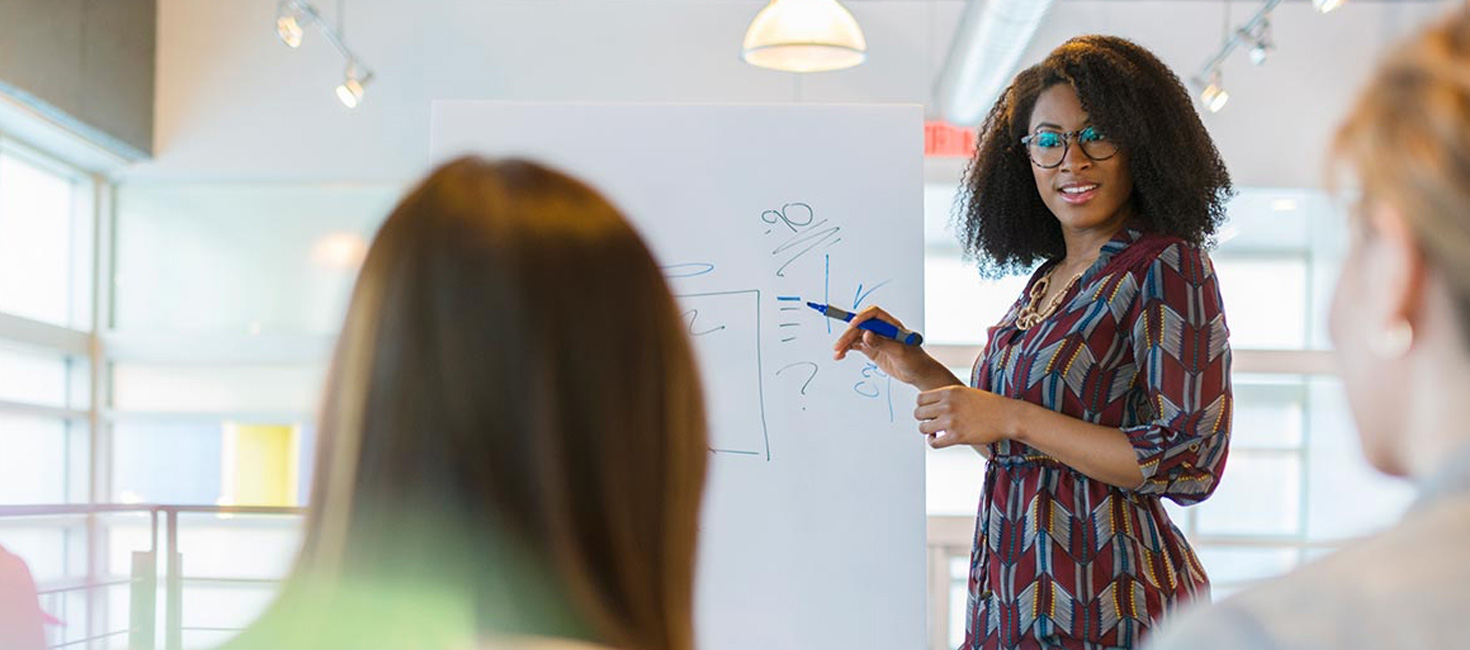 Woman writing on a white board presenting to professional colleagues