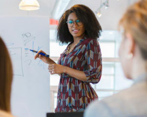 Woman writing on a white board presenting to professional colleagues